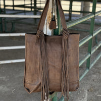 Light chocolate brown leather tote with fringe knotted around handles hanging on stall panels
