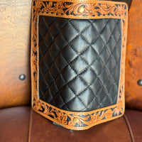 Black quilted leather organizer wallet with brown floral tooled border and black buckstitch propped up against wooden background