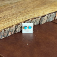 Turquoise stone earrings on a card with a wooden and leather background