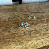 Heart shaped silver earrings with turquoise stones on a wooden surface