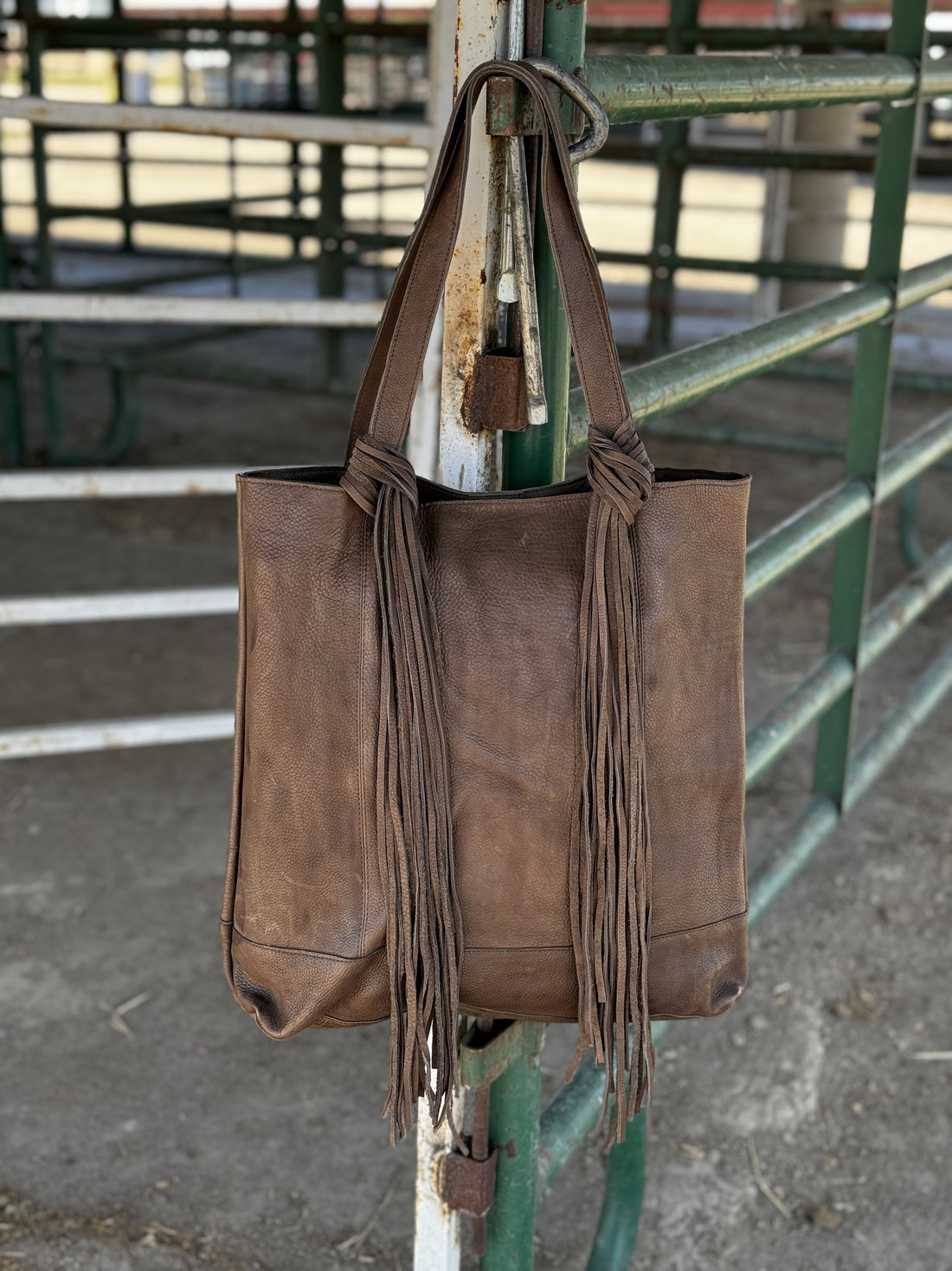 Light chocolate brown leather tote with fringe knotted around handles hanging on stall panels