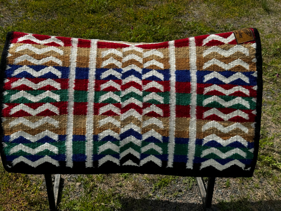 A contoured saddle blanket on saddle rack with white vertical lines and broken horizontal lines over a background of red, tan, gold, royal blue, and kelly green