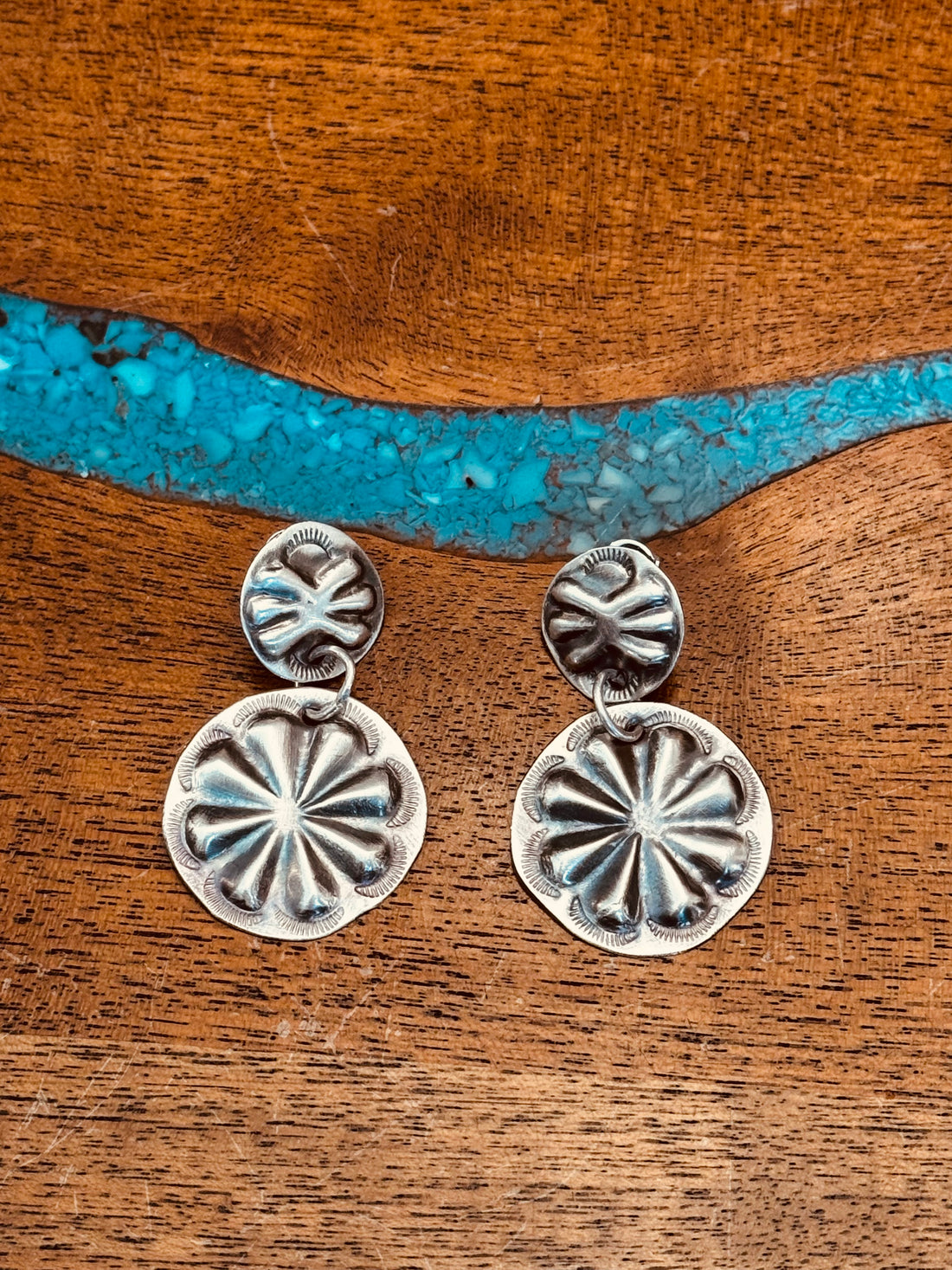 sterling silver stamped concho earrings on concho studs laying on wooden surface