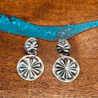 sterling silver stamped concho earrings on concho studs laying on wooden surface