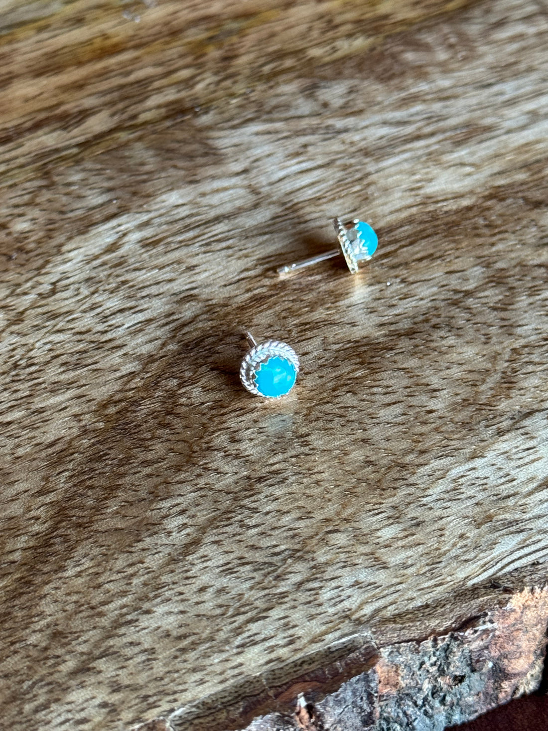 Pair of small turquoise gemstone earrings on a wooden surface