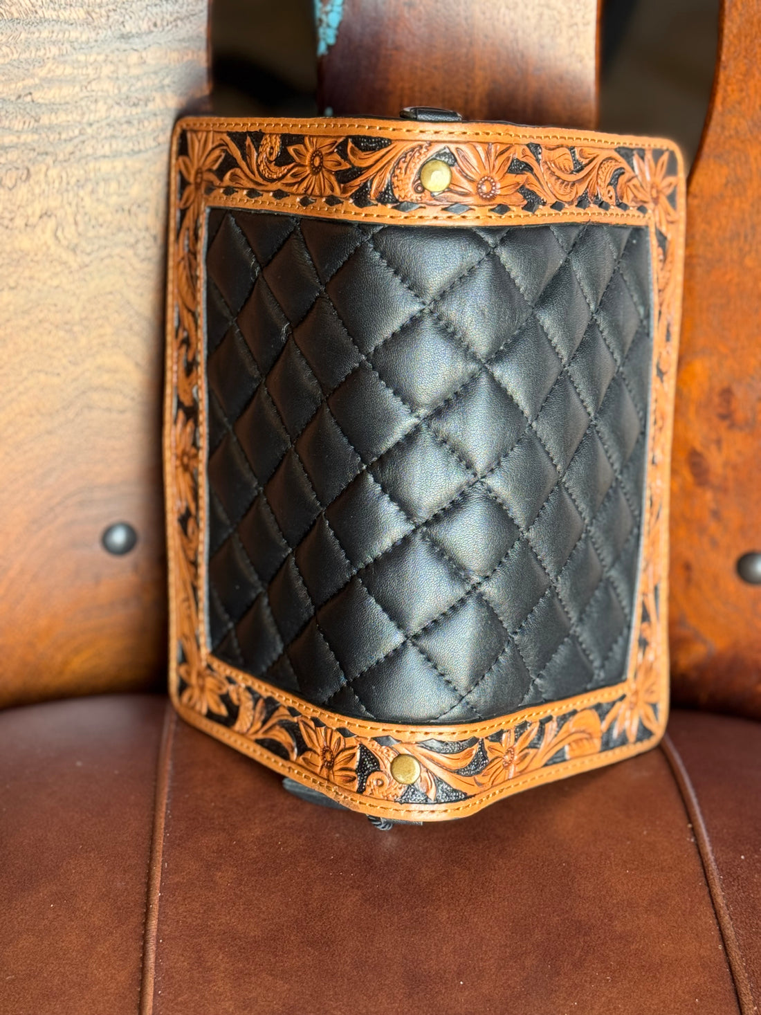 Black quilted leather organizer wallet with brown floral tooled border and black buckstitch propped up against wooden background