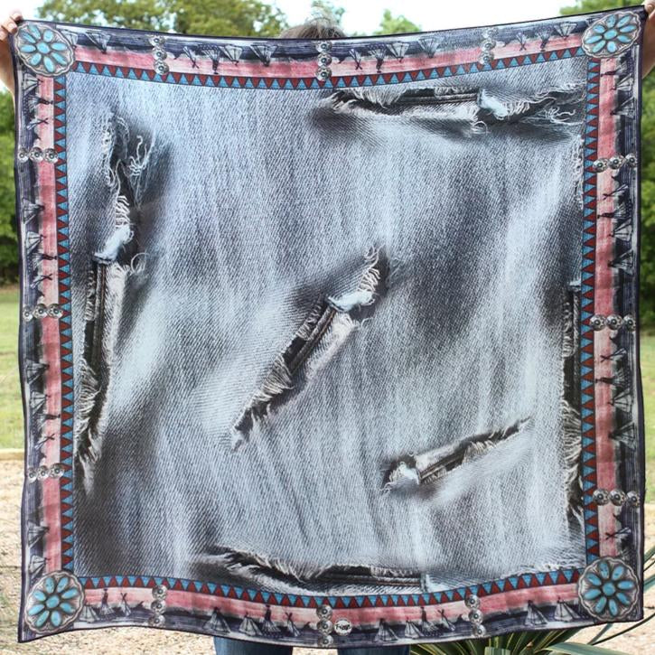 A silk charmeuse scarf with a distressed denim pattern, featuring red and dark blue aztec border and turquoise conchos as accent, displayed on a person.