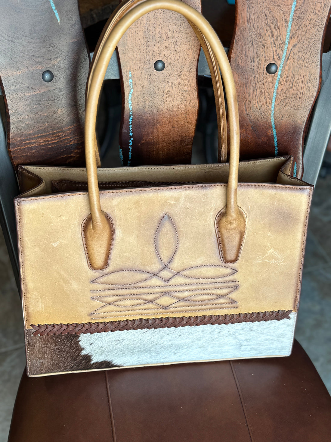 distressed light brown leather brief case with brown boot stitch design and hair on hide strip along bottom of bag, with leather whipstitching, and tall stand up handles