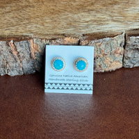 Pair of turquoise earrings on a card against a wooden background
