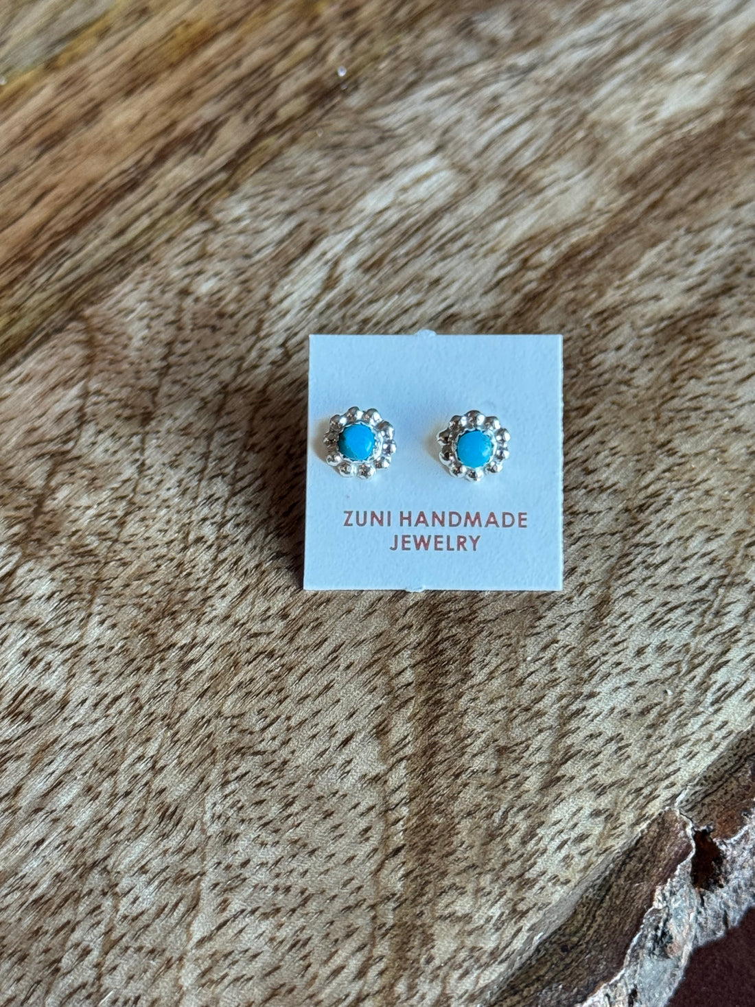 Pair of turquoise stud earrings on a Zuni Handmade Jewelry card, placed on a wooden surface.