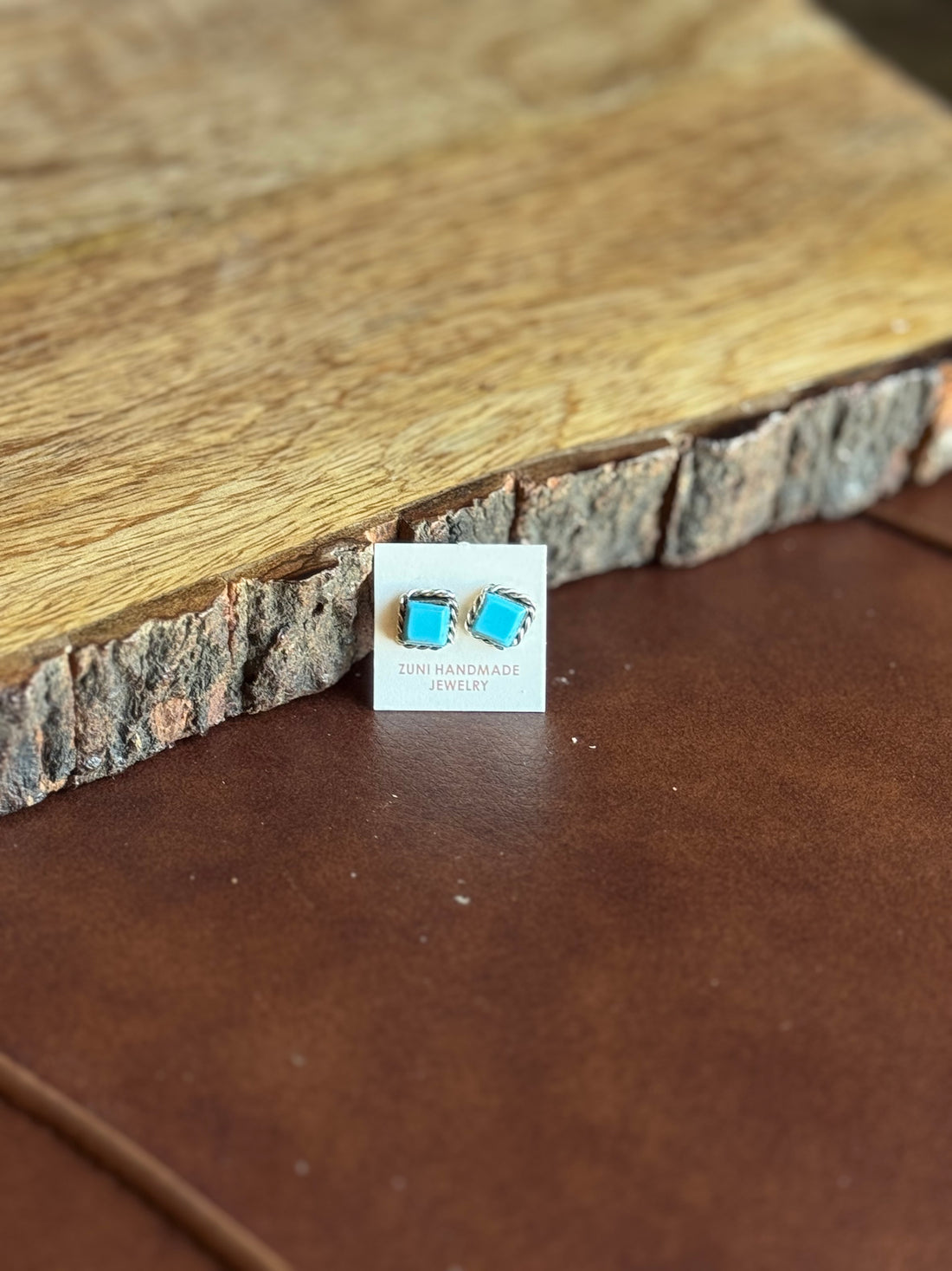 Turquoise stone earrings on a card with a wooden and leather background