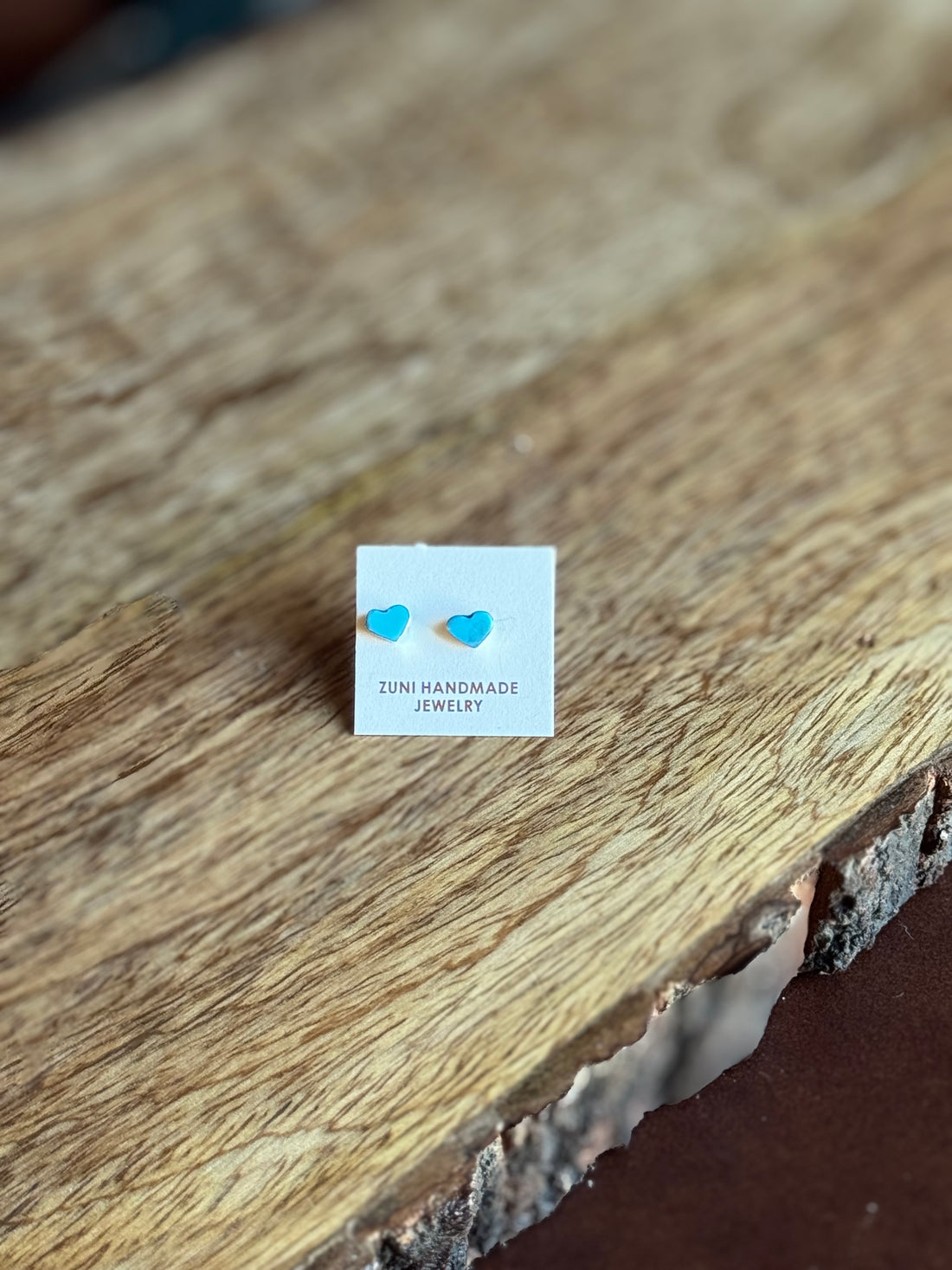 Pair of heart-shaped earrings on a 'Zuni Handmade Jewelry' card on a wooden surface.