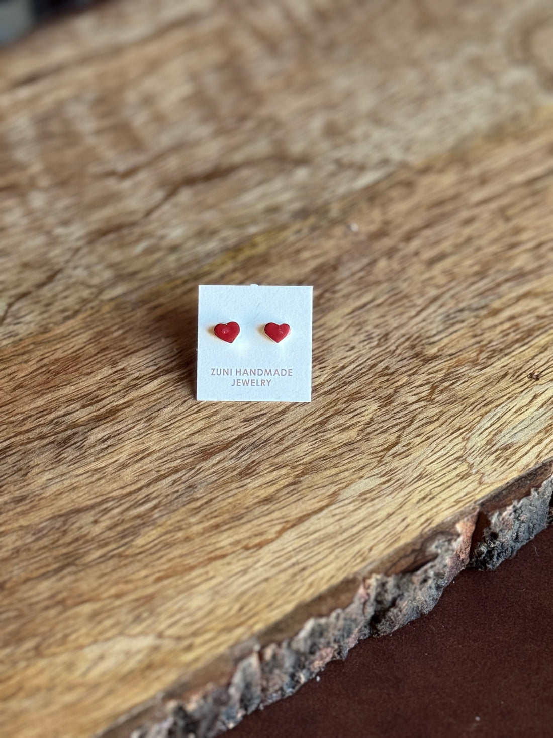 Red heart-shaped earrings on a white card with 'Zuni Handmade Jewelry' text, placed on a wooden surface.