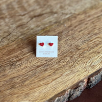 Red heart-shaped earrings on a white card with 'Zuni Handmade Jewelry' text, placed on a wooden surface.