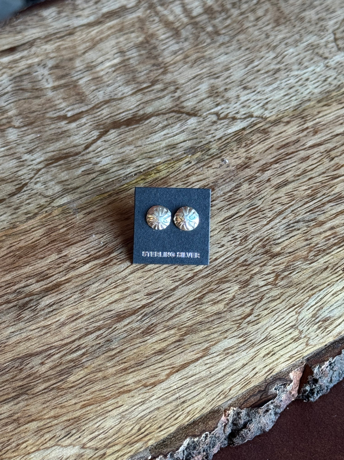 Pair of silver earrings on a black card with a wooden surface background