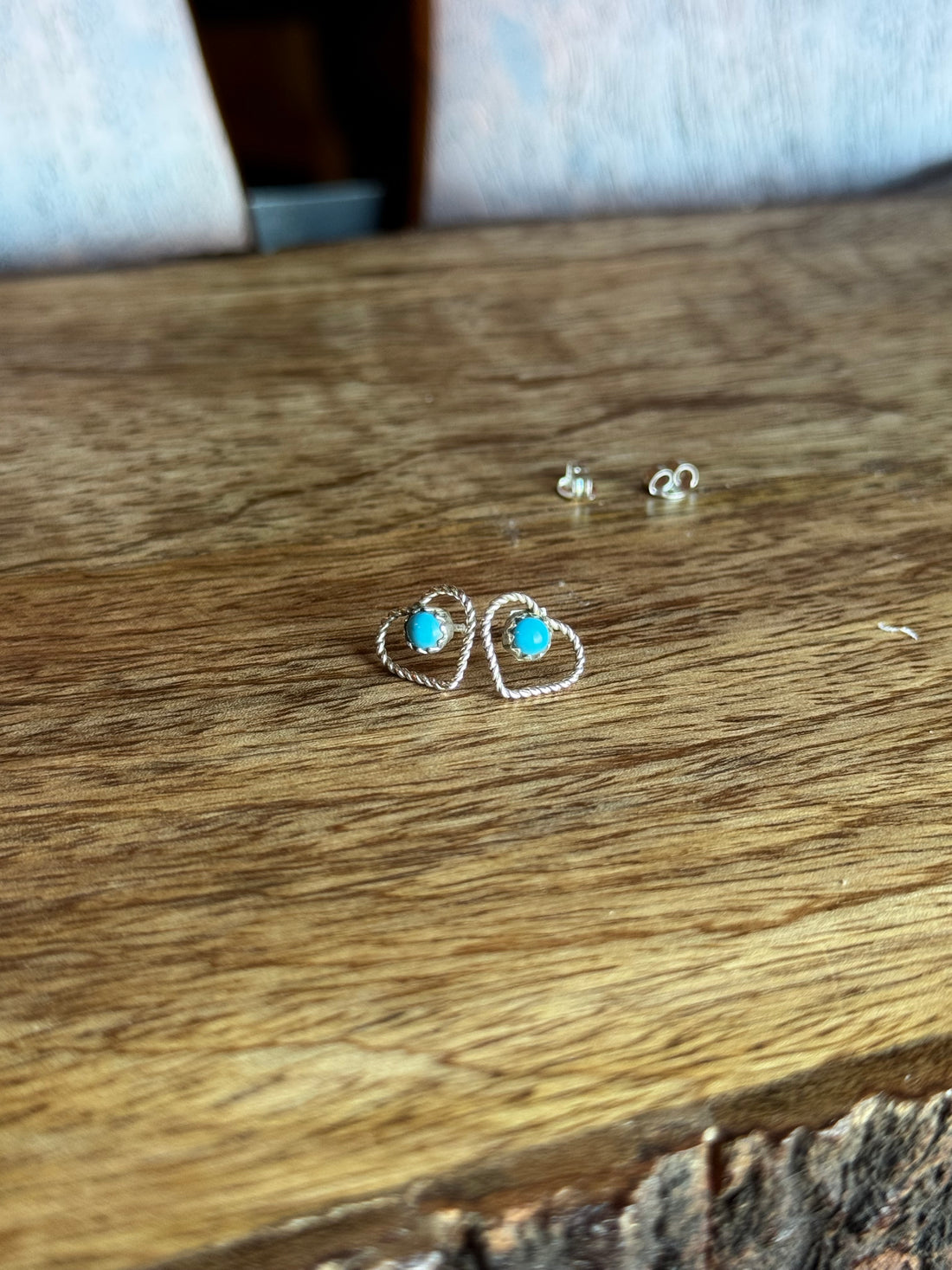 Heart shaped silver earrings with turquoise stones on a wooden surface