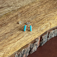 Small turquoise gemstone earrings on a wooden surface