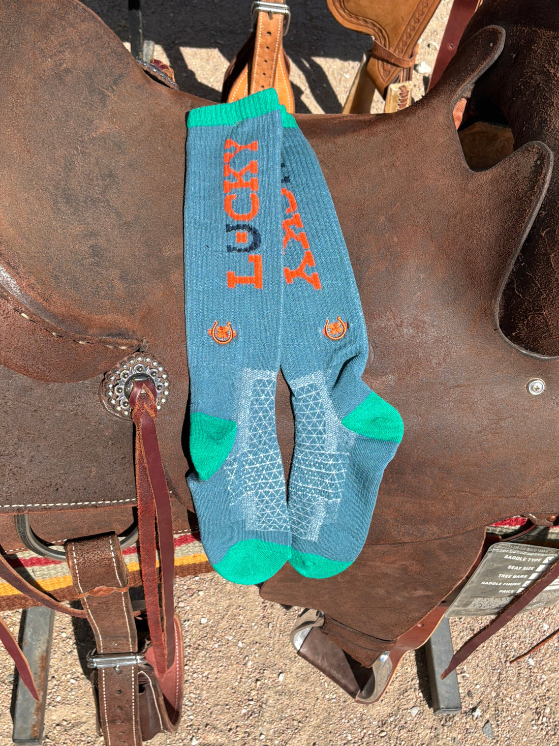 Pair of blue socks with orange text on a brown leather saddle